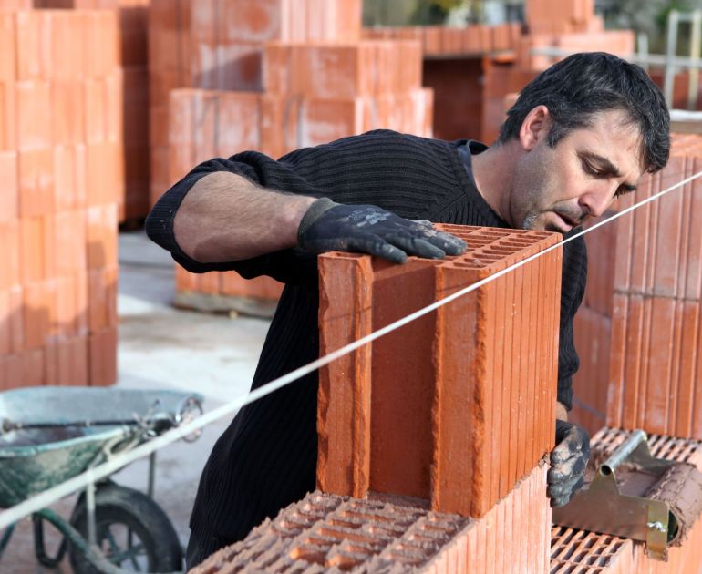 Mason laying brick along a level guide line